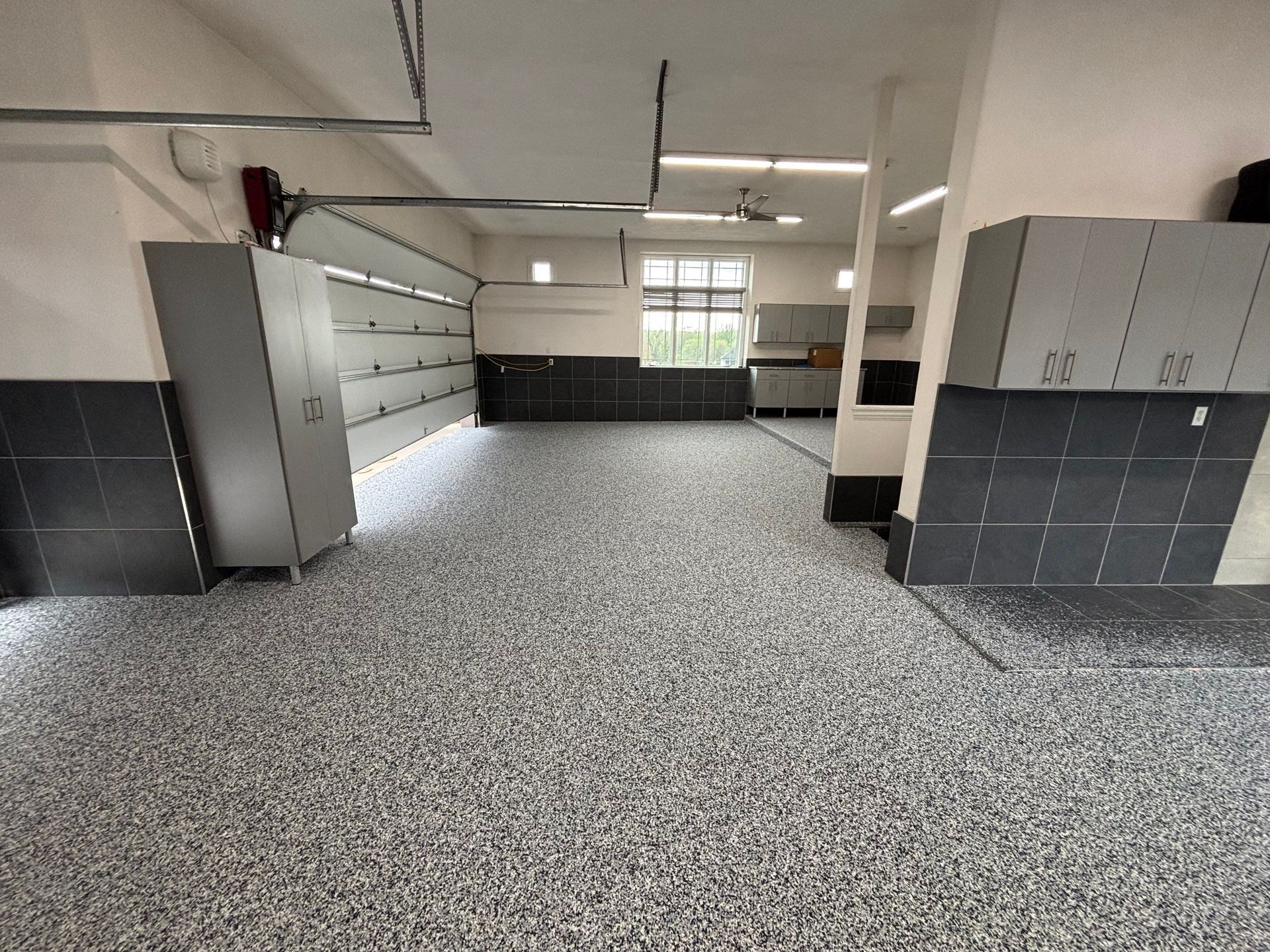 Empty industrial garage with gray floor, white walls, lockers, and cabinets along the sides