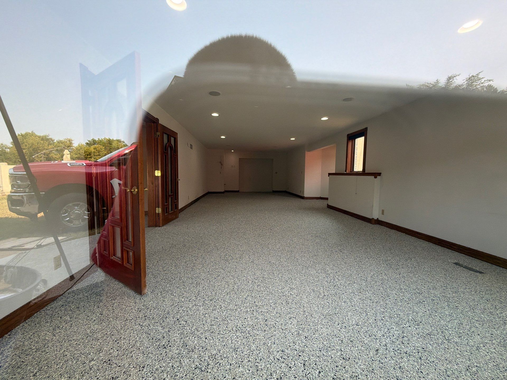 Empty carpeted room with white walls, recessed lights, and an open wooden door by a windowed entrance.