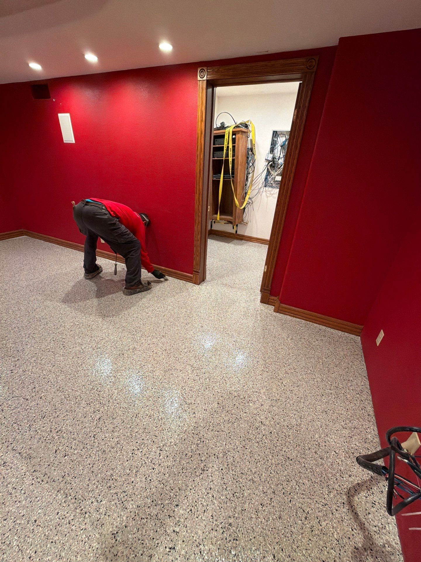 Person bending over in a red-painted room with a speckled floor near a doorway and hanging clothes.