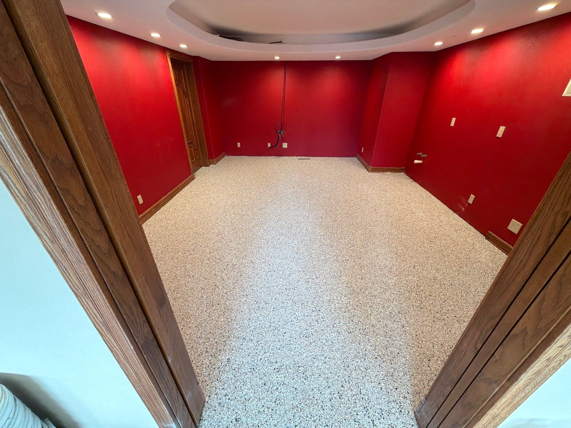 Empty room with red walls, recessed ceiling lights, and speckled carpet floor.