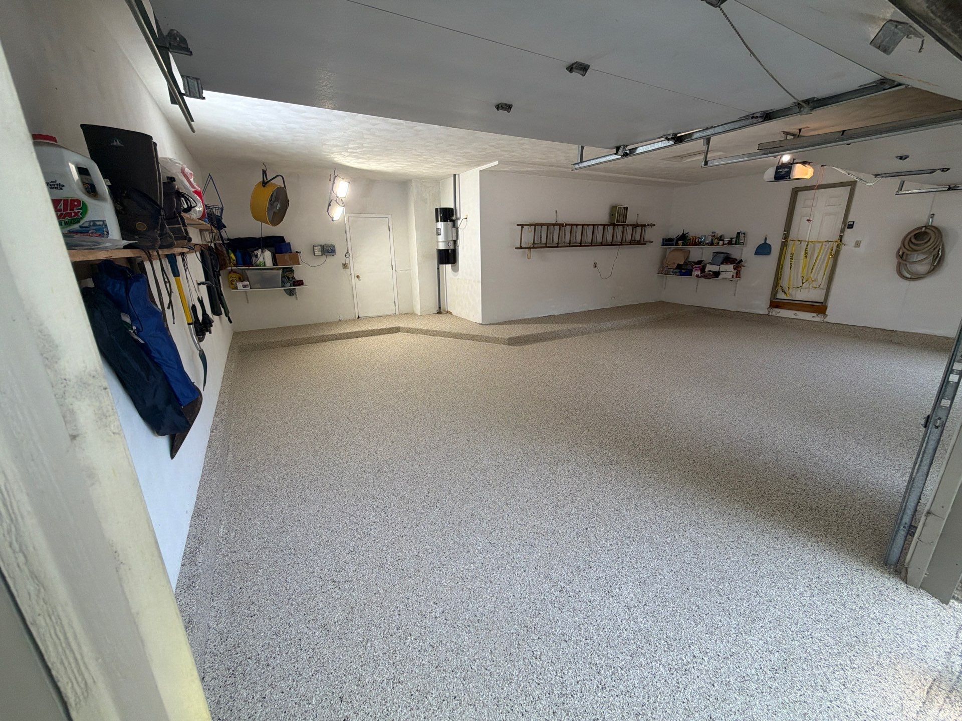 Wide empty garage with speckled floor, white walls, shelves, and hanging tools, viewed from the doorway
