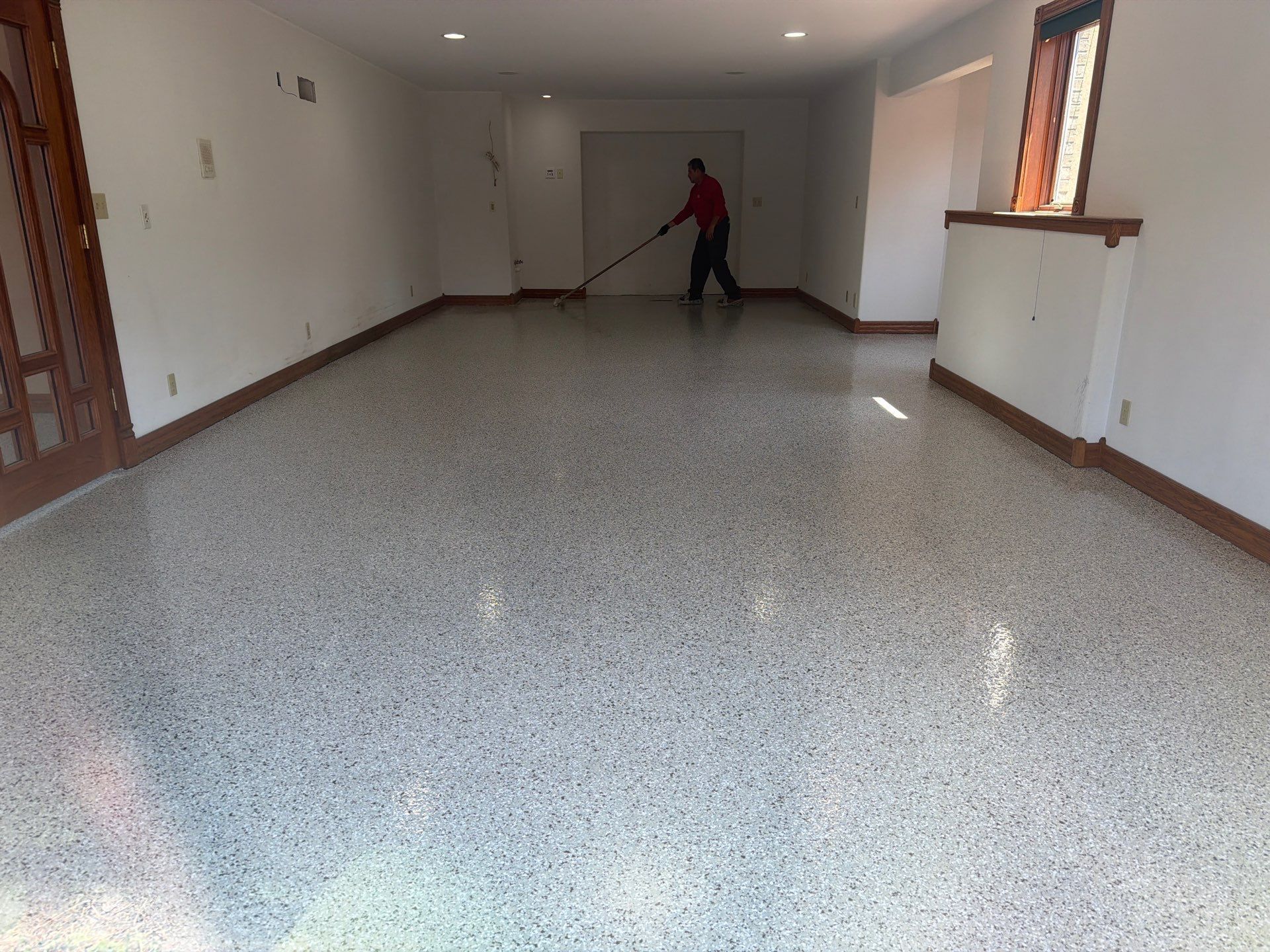 Empty carpeted room with white walls and a person near the back holding a long-handled tool.