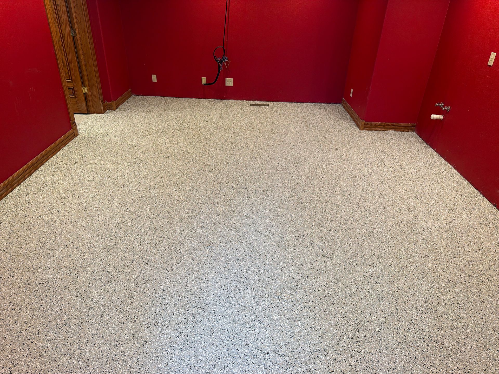 Empty speckled floor in a red-walled room with a doorway on the left.