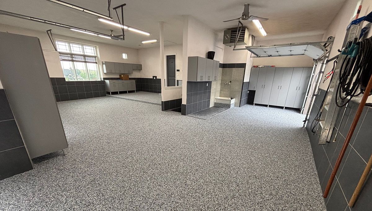 Spacious empty garage with speckled epoxy floor, support columns, windows, and a closed white overhead door.