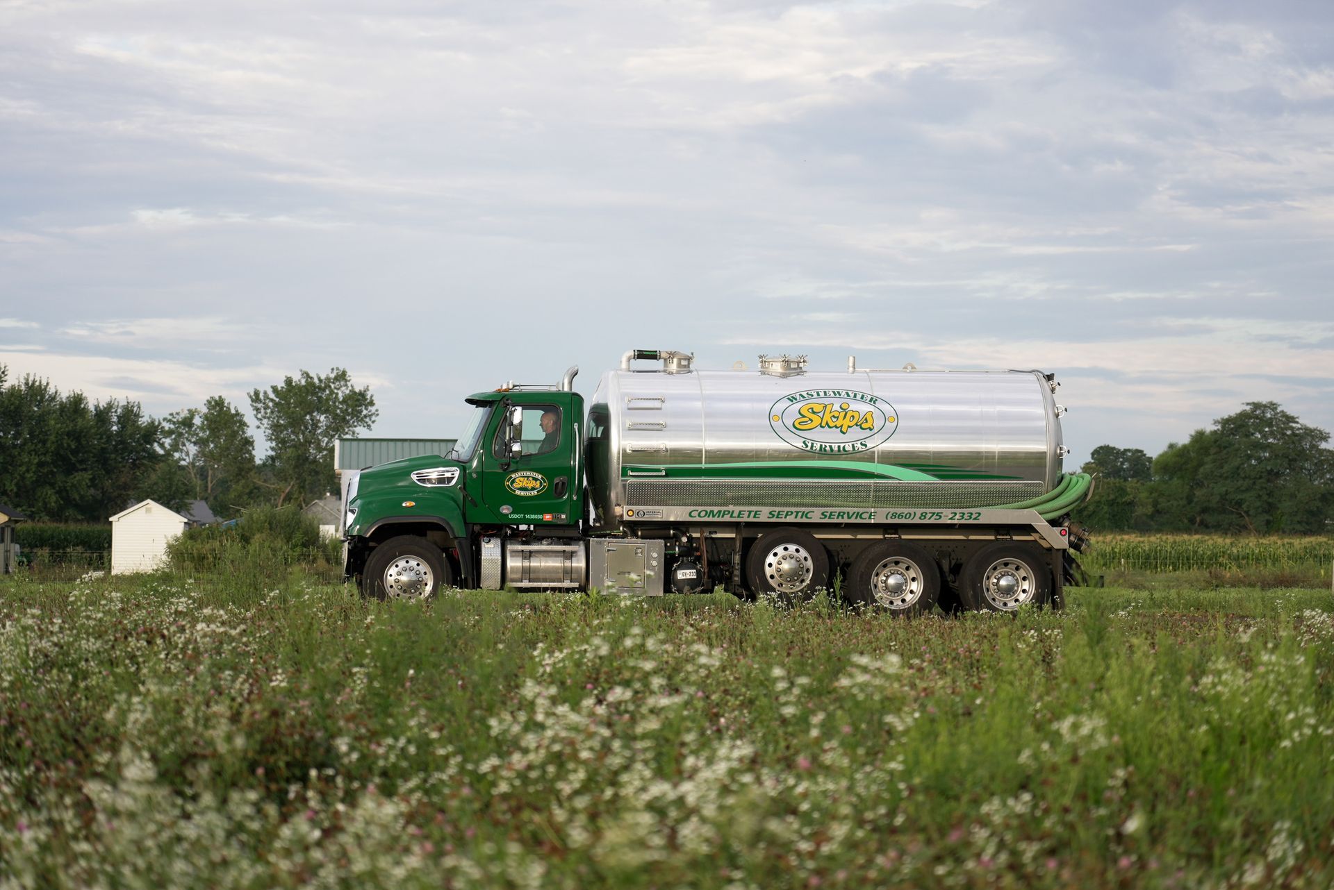 Green tanker truck in a field with a cloudy sky background.