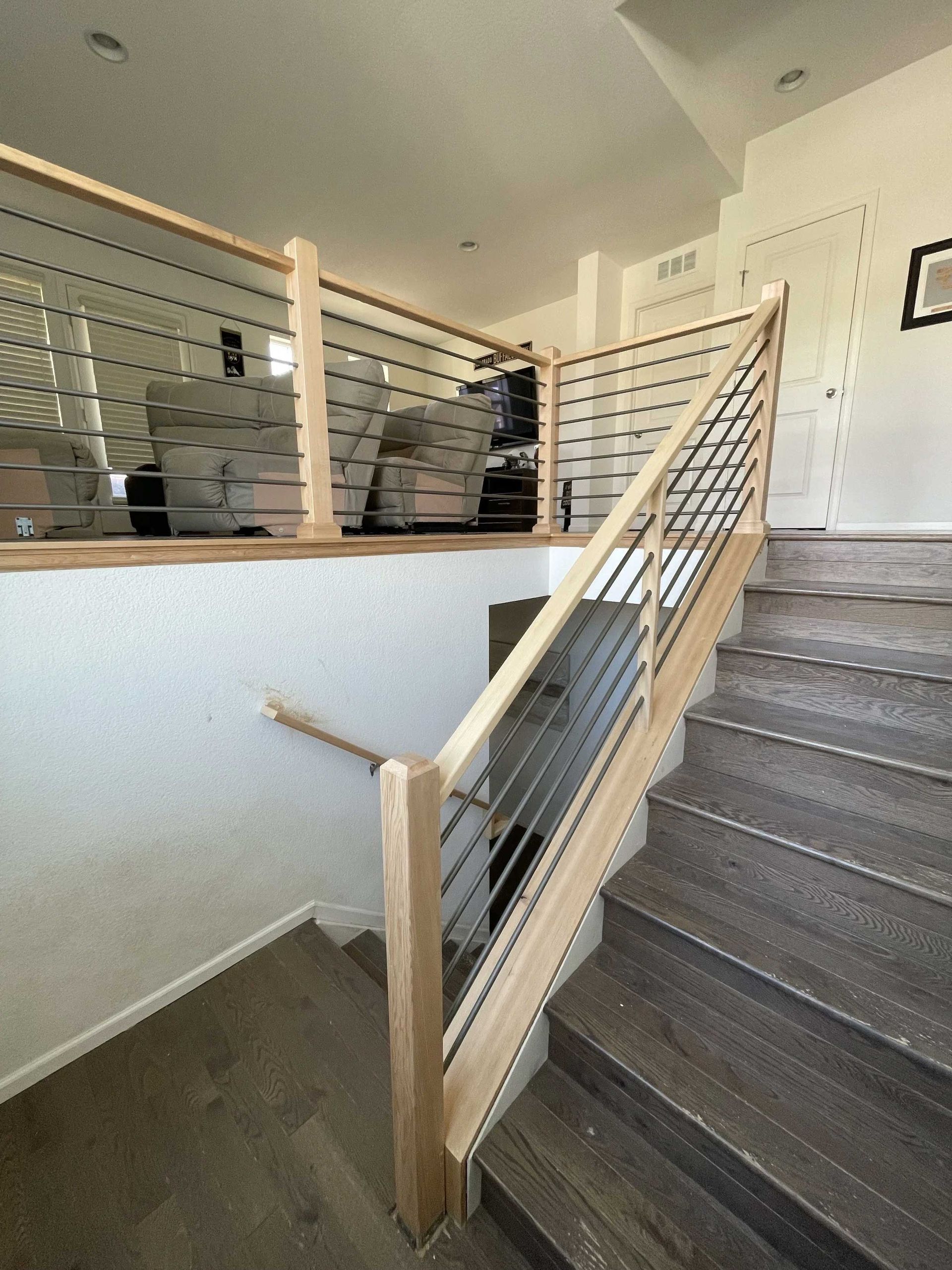 Staircase with wooden handrails and metal cable balustrade. Neutral walls, natural wood, and gray steps.