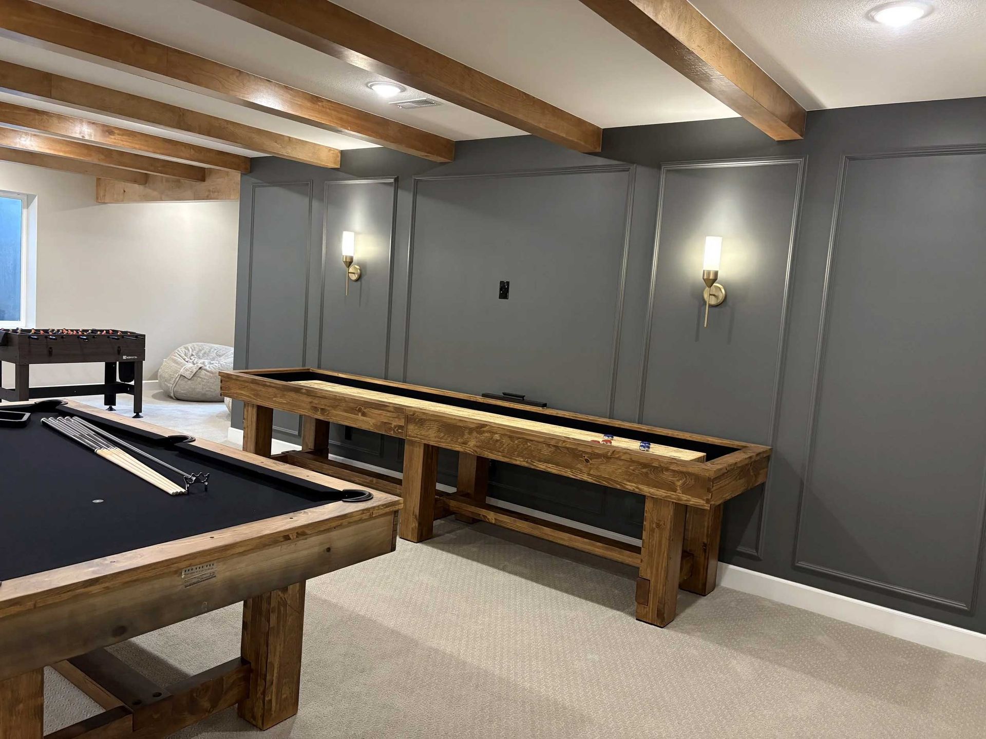 Recreation room with pool table, shuffleboard, and gray walls with sconces. Beige ceiling beams and carpet.
