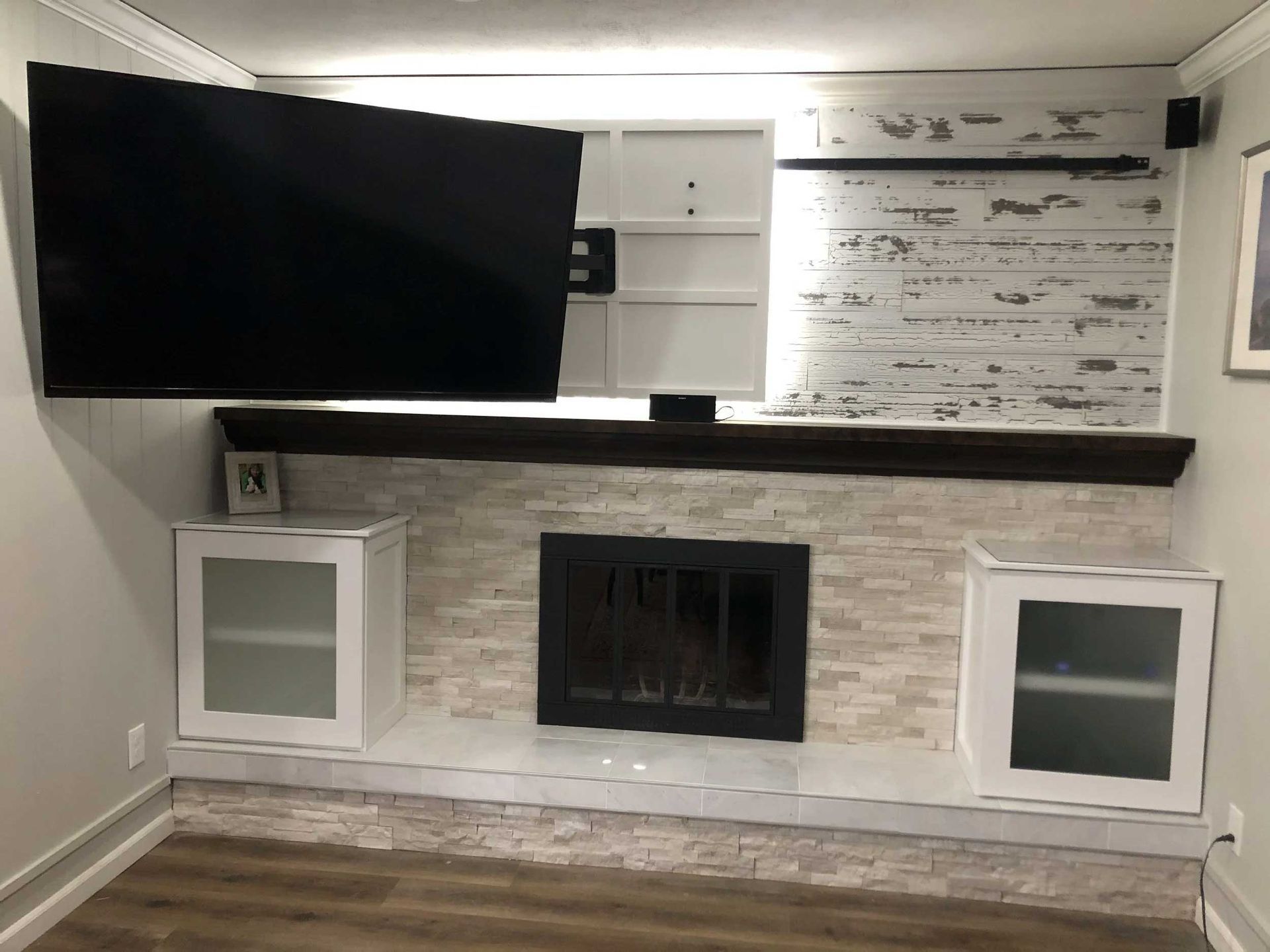 Fireplace with mounted TV, flanked by white cabinets. Features include a brick backdrop, dark mantel, and wood flooring.