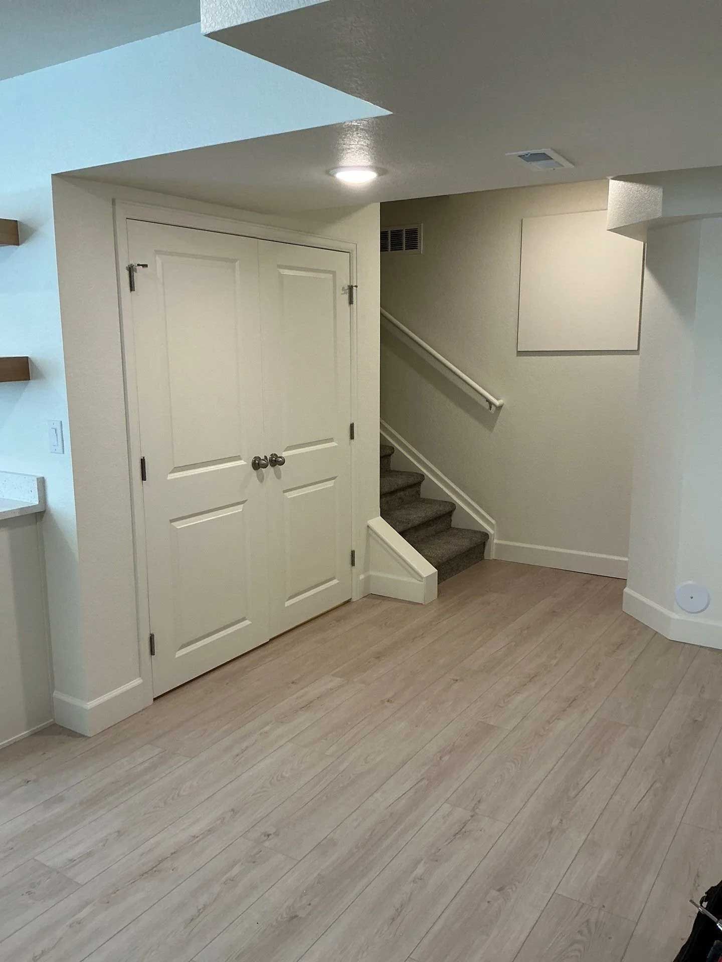 Basement with a closed white door, staircase, and light wood flooring.