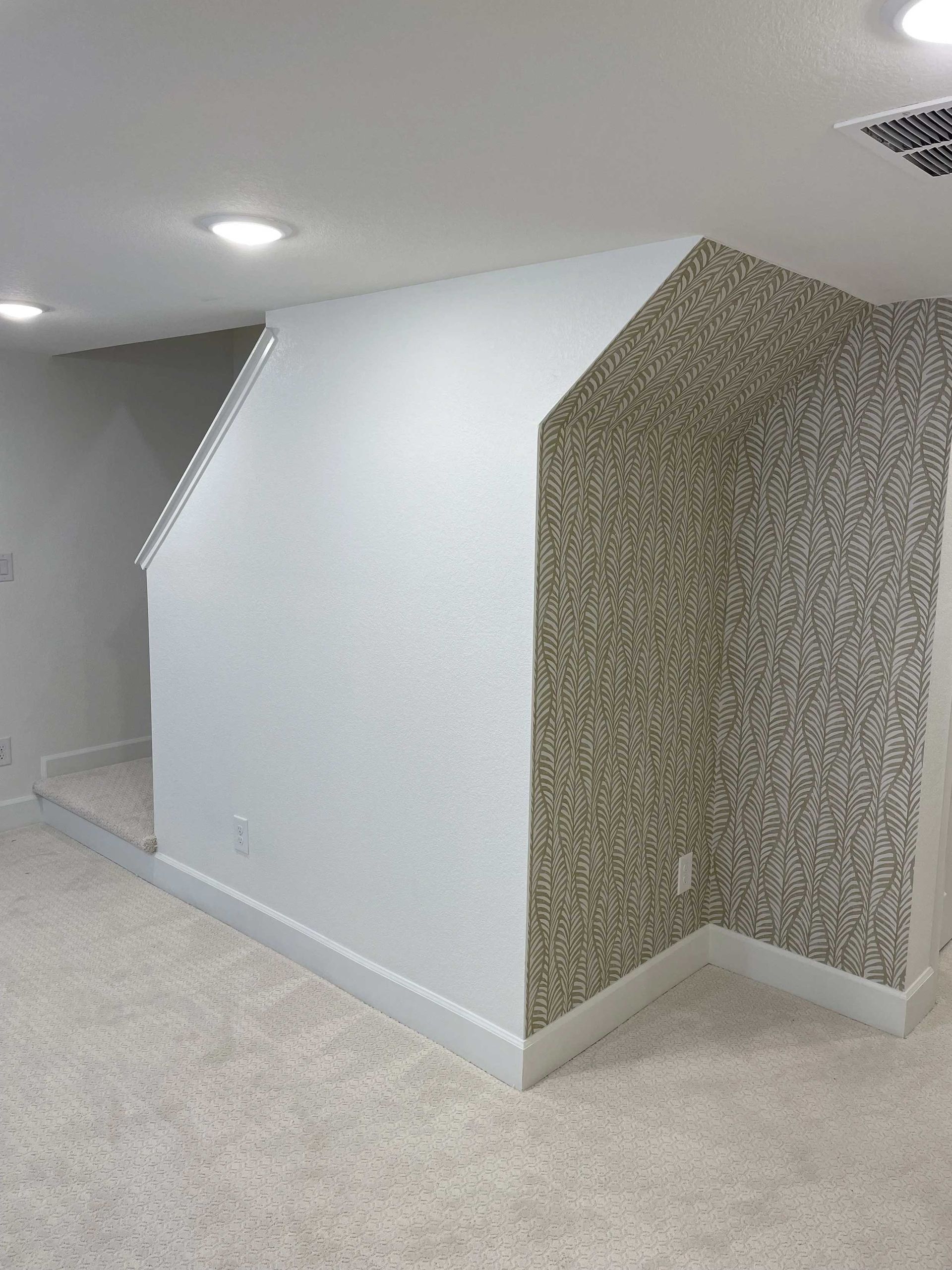 White wall with patterned wall on the right side and beige carpet, under ceiling lights.