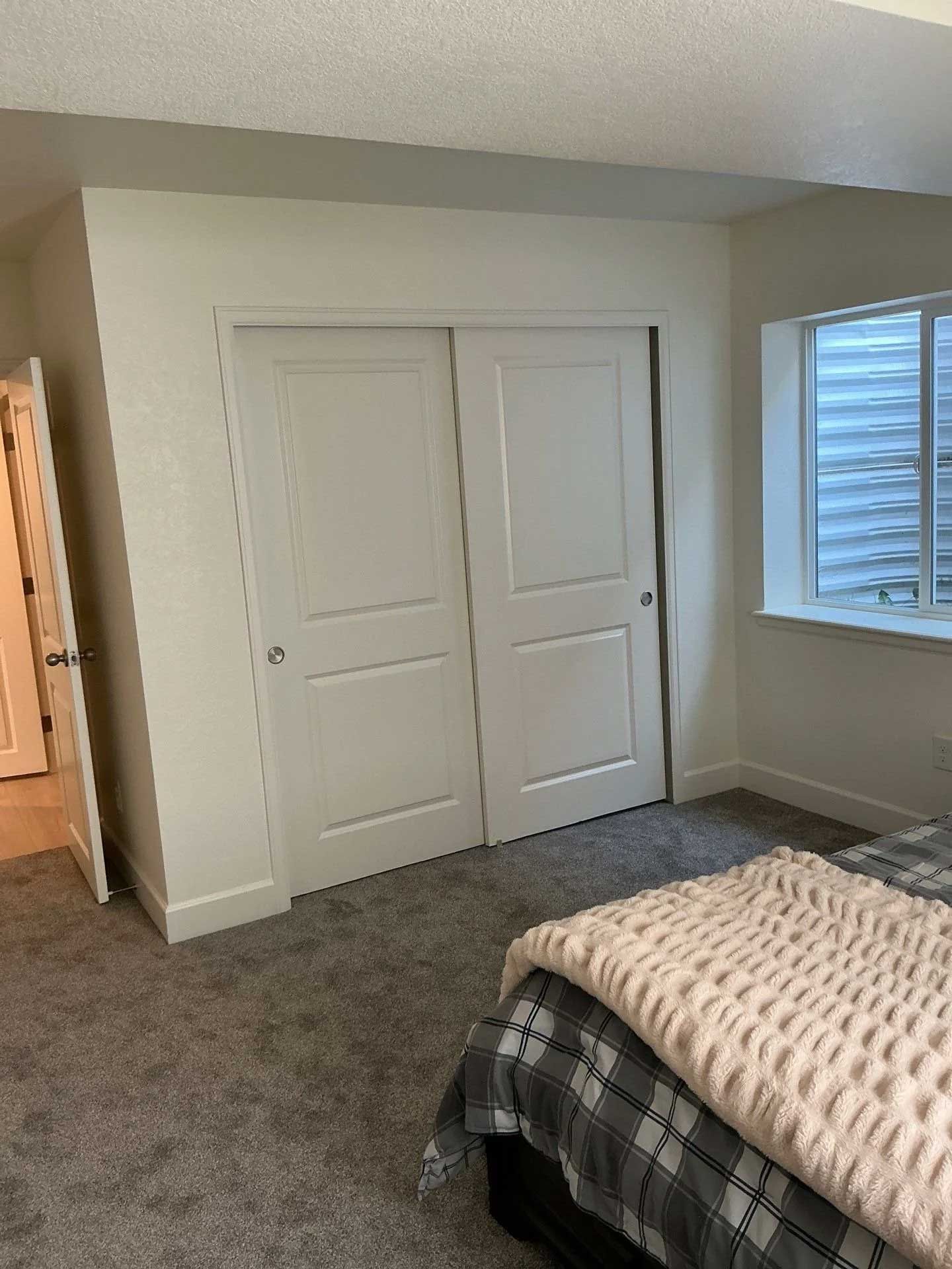Bedroom with closet doors, window, bed with plaid blanket, and carpeted floor.