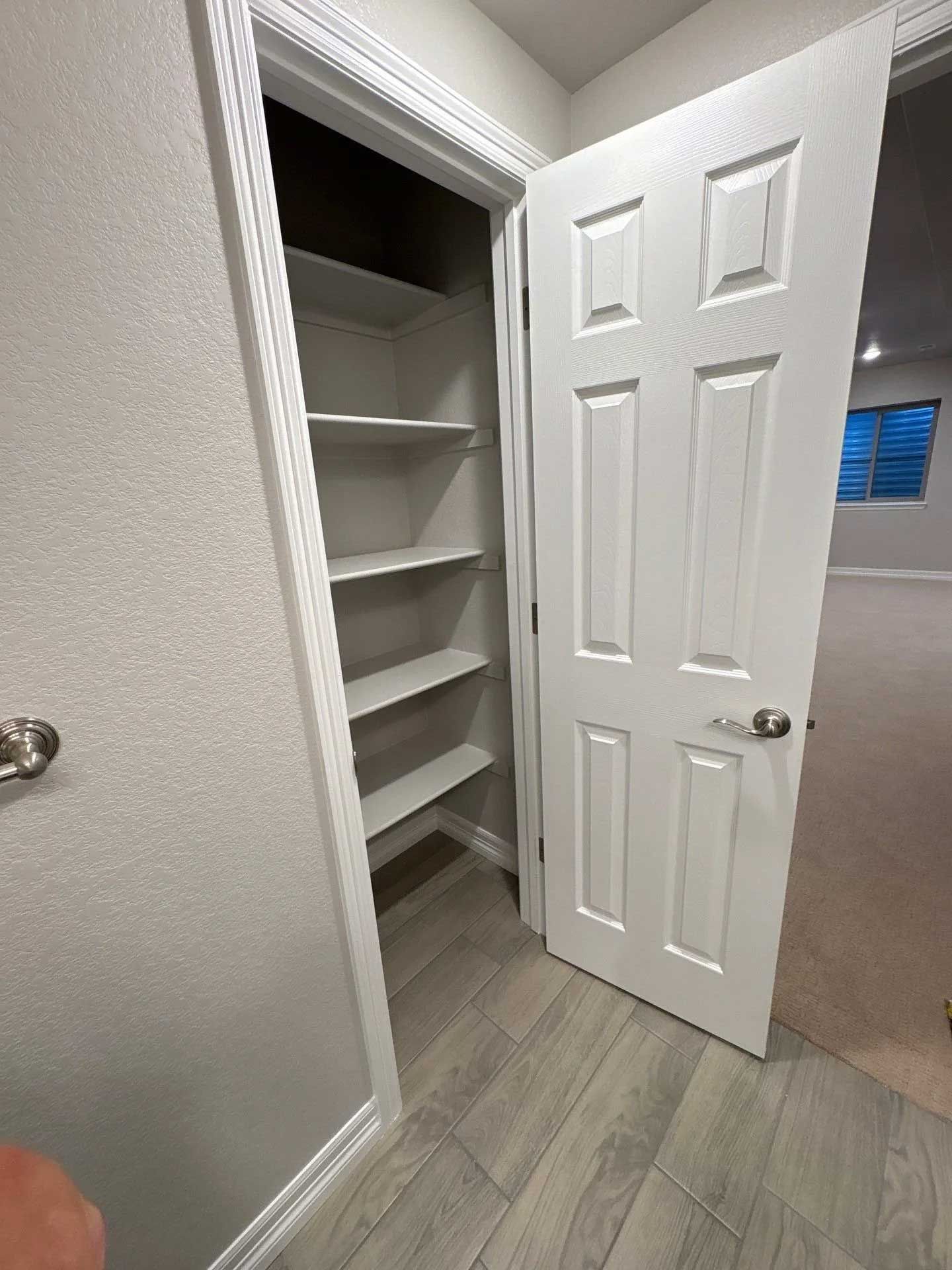 A closet with white shelves and door open to a carpeted room.