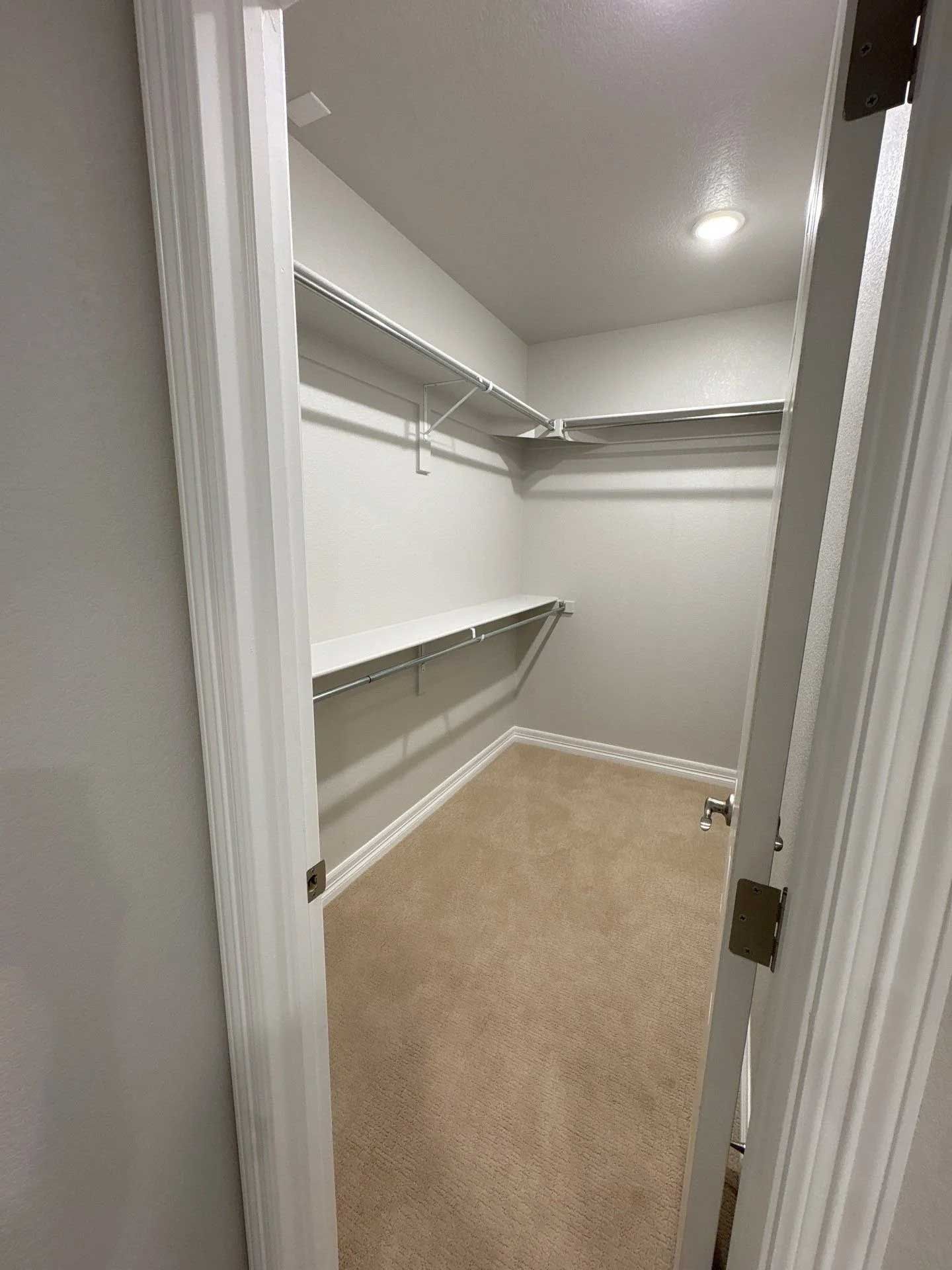 A small, empty walk-in closet with shelves and beige carpet, viewed through an open doorway.