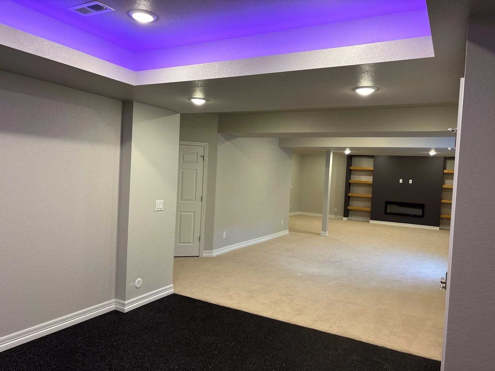 Basement interior with black floor, light carpet, recessed lighting, and a fireplace in the distance.