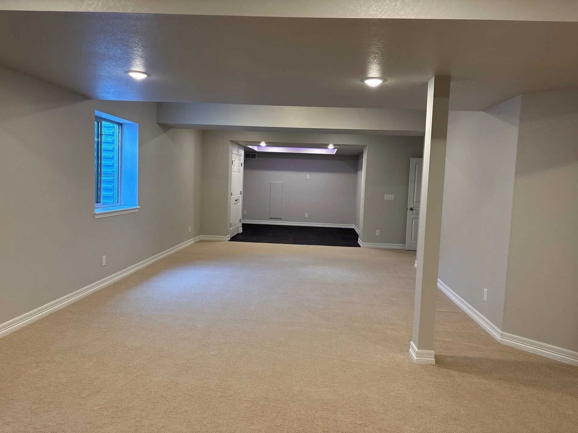 Empty, beige carpeted basement with gray walls, recessed lighting, and a small window.