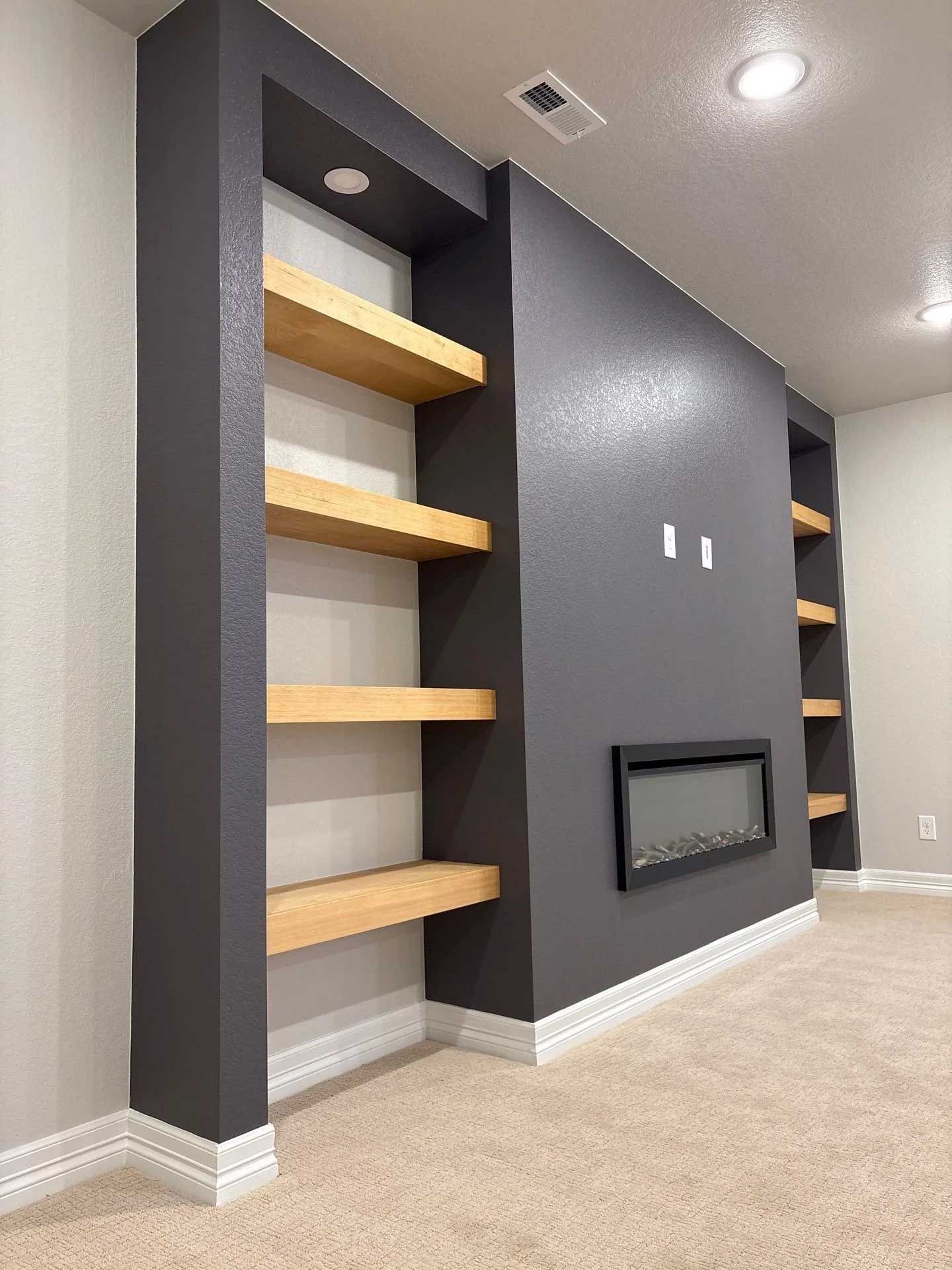 Built-in shelves with wood shelving, dark grey framing, and a fireplace on a grey wall, with a beige carpet.