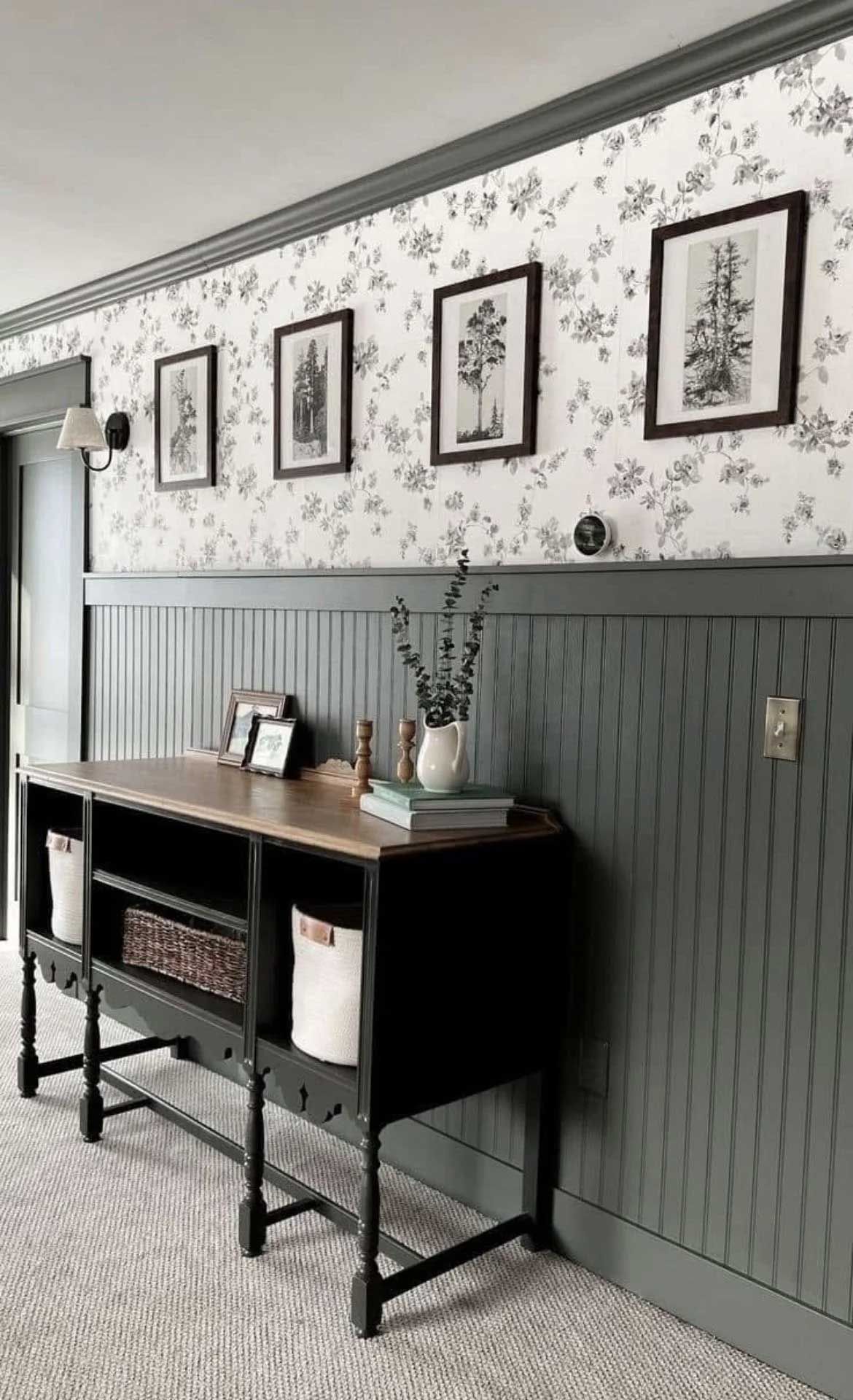 A hallway with floral wallpaper, wainscoting, and a black console table with framed art.