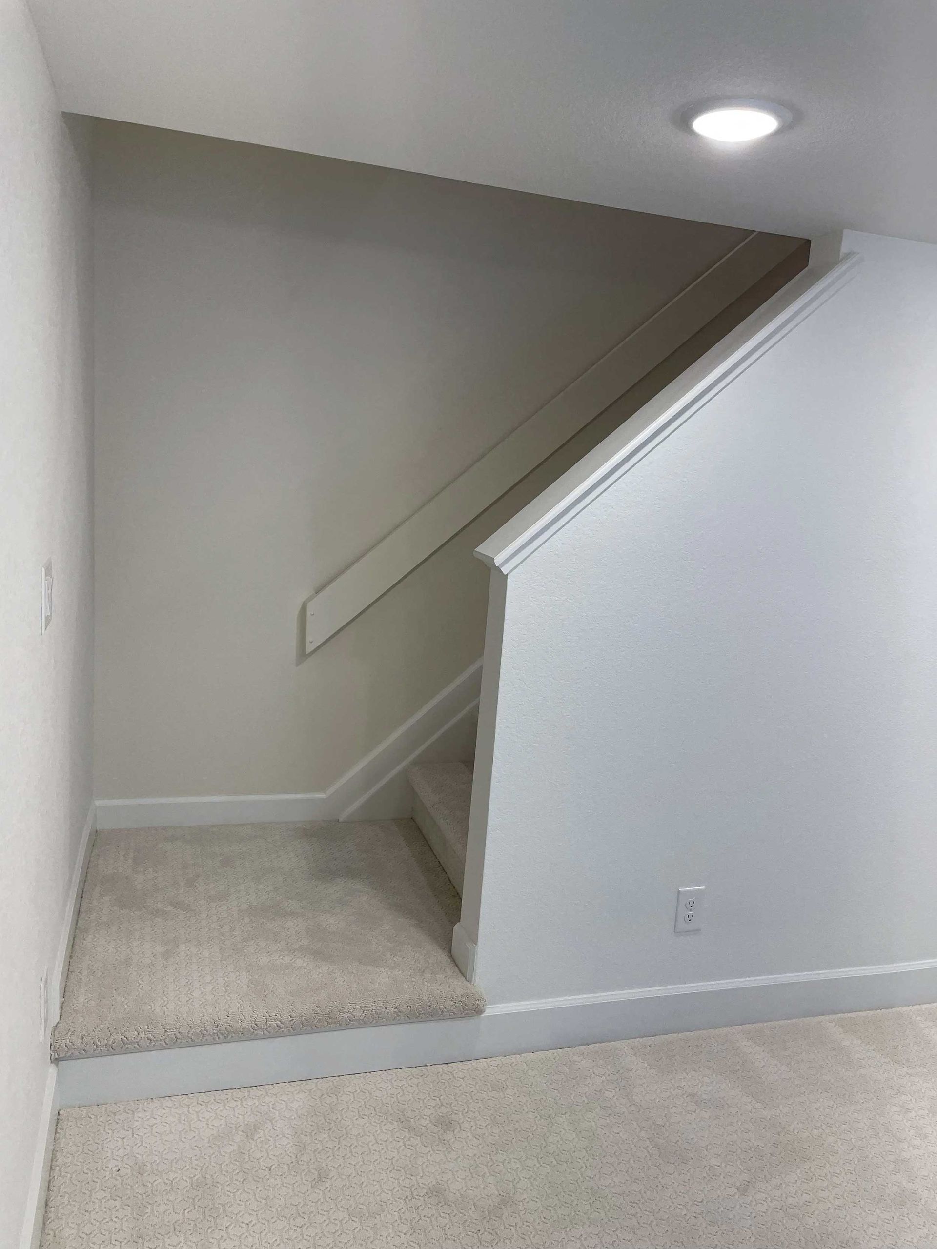Staircase in a home with carpeted steps and a white handrail. Walls are painted white.