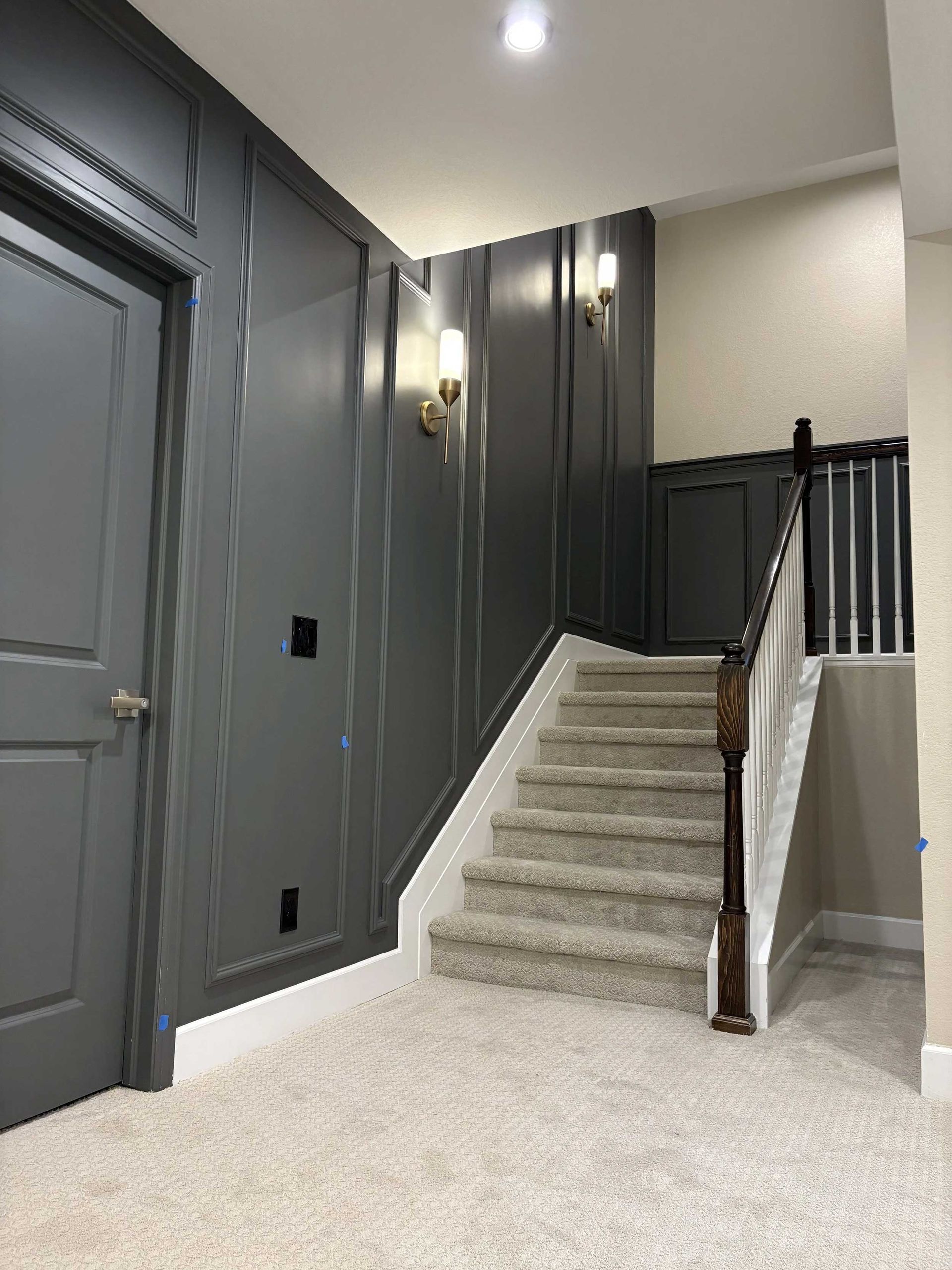 A staircase with gray paneling and carpet. A gray door is on the left.