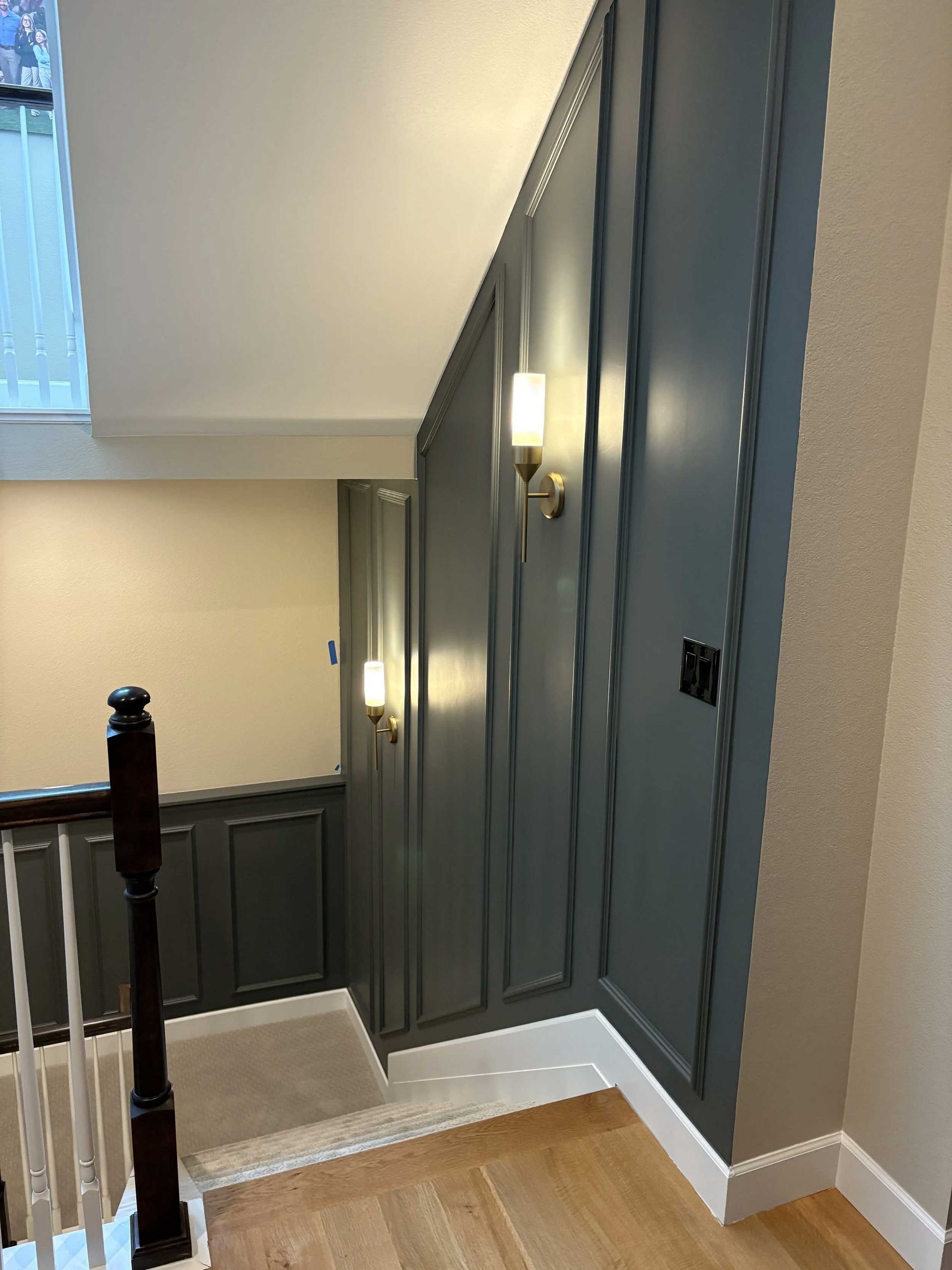 Stairwell with gray paneling, sconce lighting, and wooden floor. Railing on left.