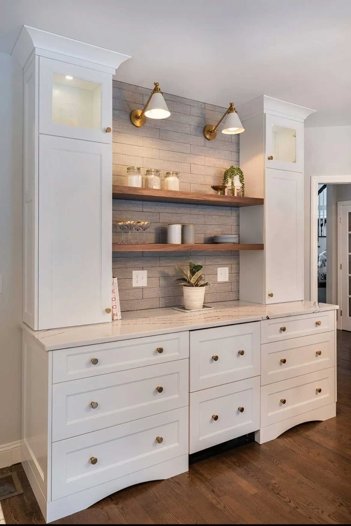 White built-in cabinets with a wood shelf and accent wall, featuring gold sconces and marble countertop.