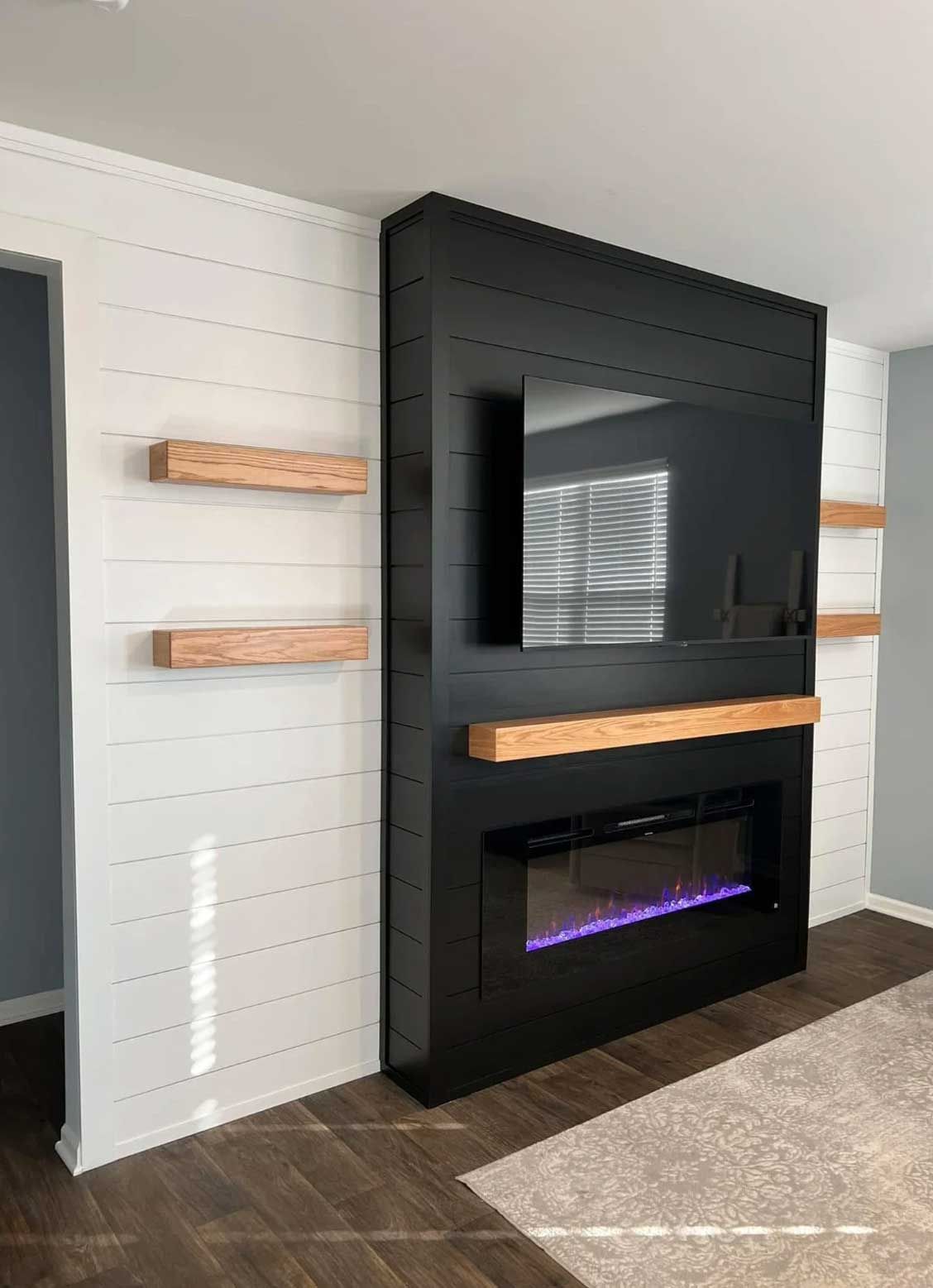 Modern black fireplace with mounted TV and wooden shelves on white shiplap wall.