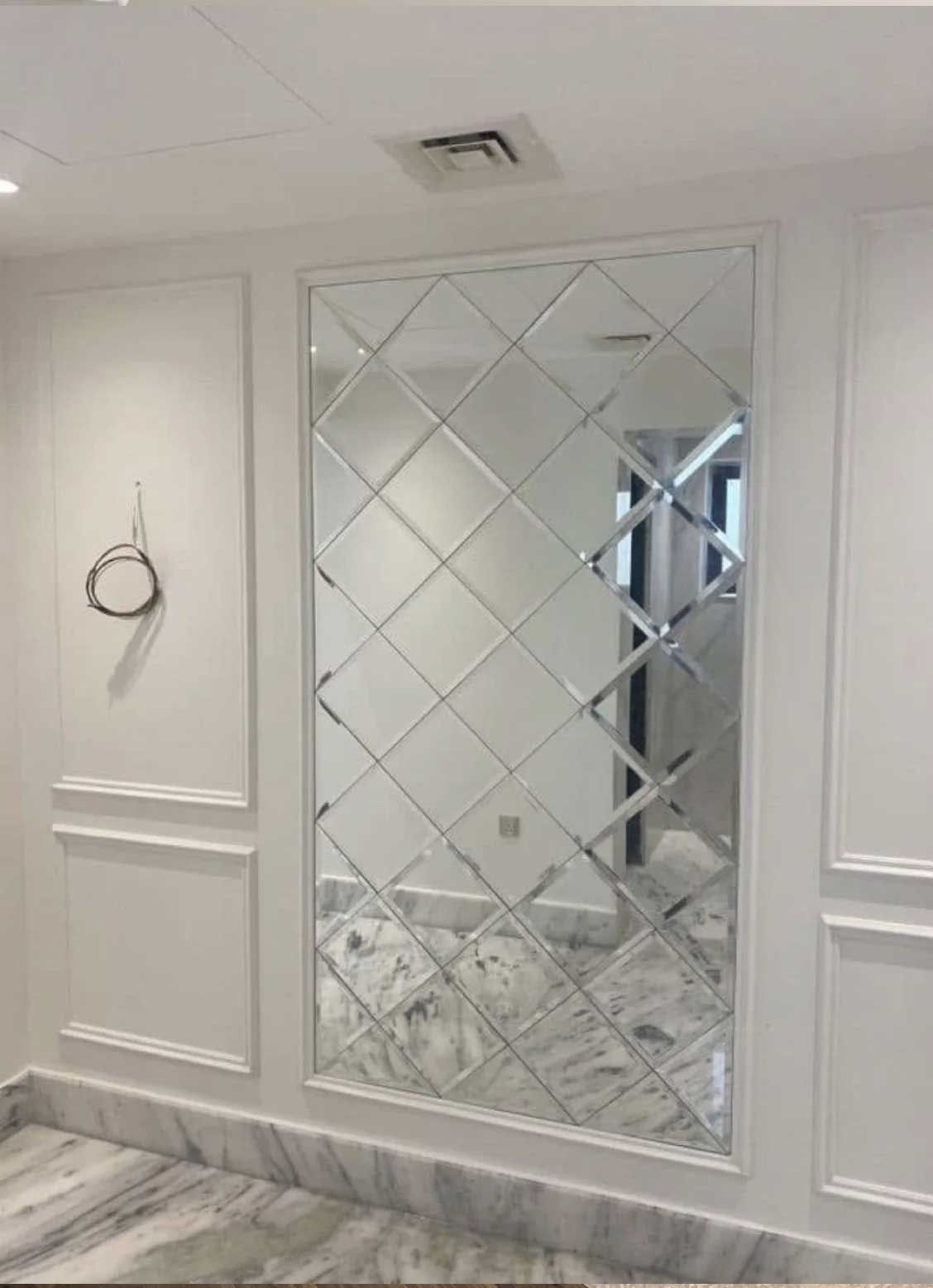Large diamond-patterned mirror on white wall, framed, in a room with marble floor and decorative molding.