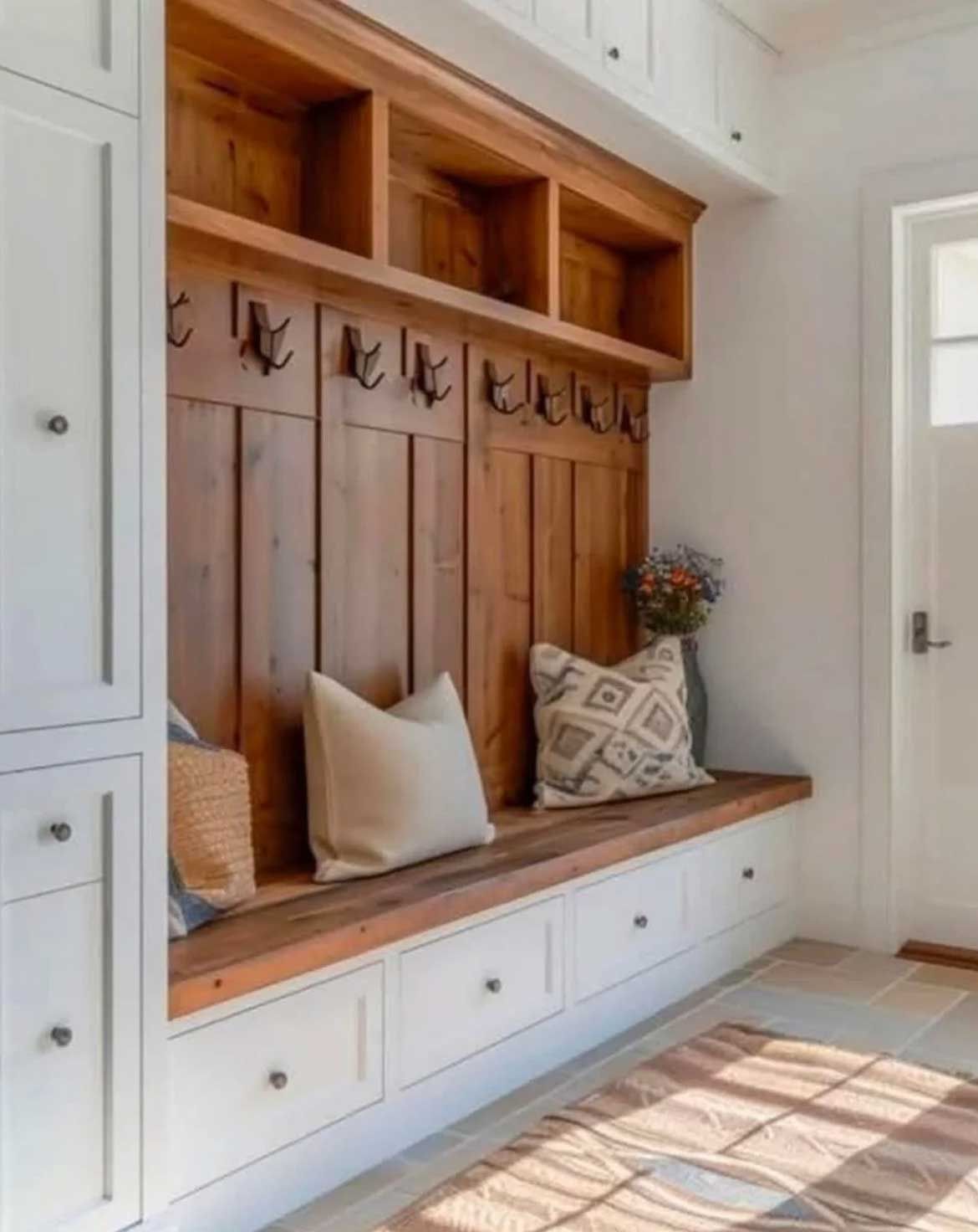 Mudroom with wood bench, storage, and hooks. White cabinets, brown wood, and neutral cushions.
