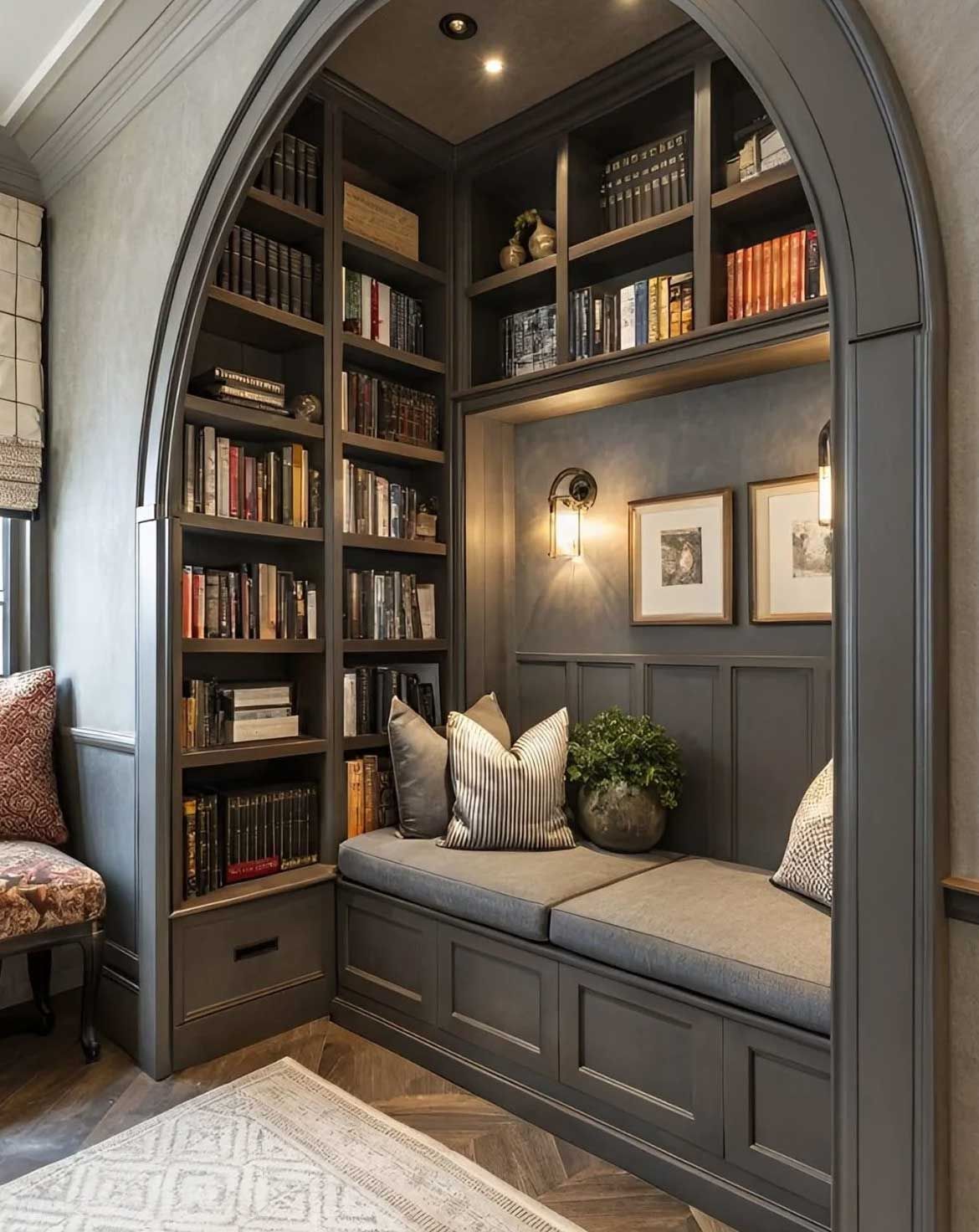 Cozy reading nook with built-in bookshelves, cushioned bench, and arched doorway. Dark gray walls, books, pillows, and two framed pictures.