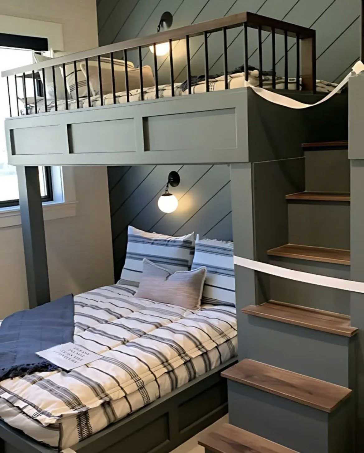 Two-level bunk bed in a gray-green room. Top bunk has railing; stairs on the side.