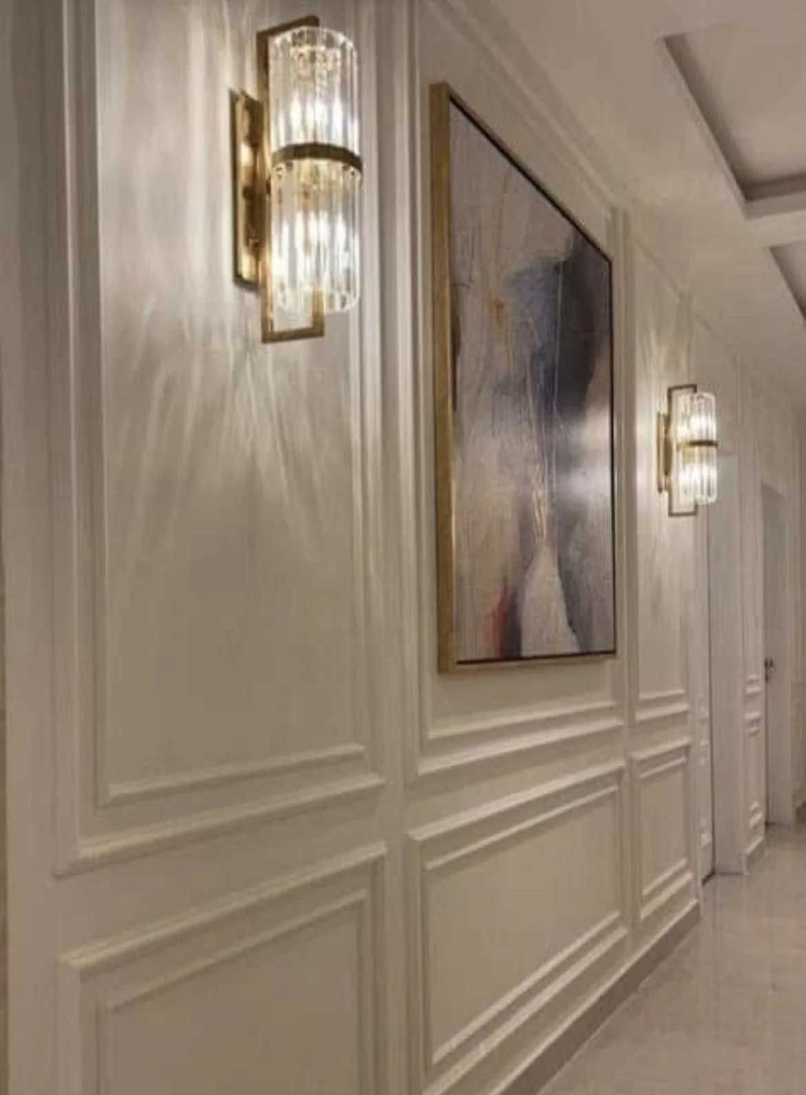 A hallway with white paneling, wall sconces, and an abstract painting.