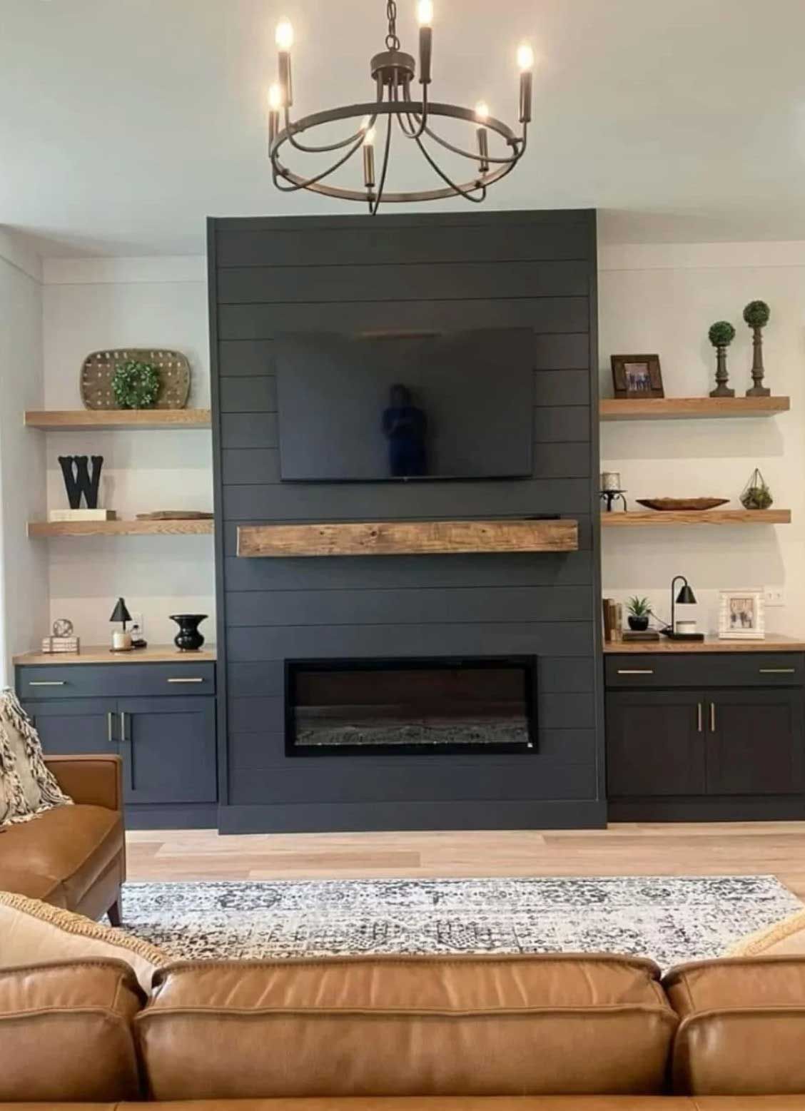 Living room with dark gray shiplap fireplace, floating shelves, and brown leather couch.