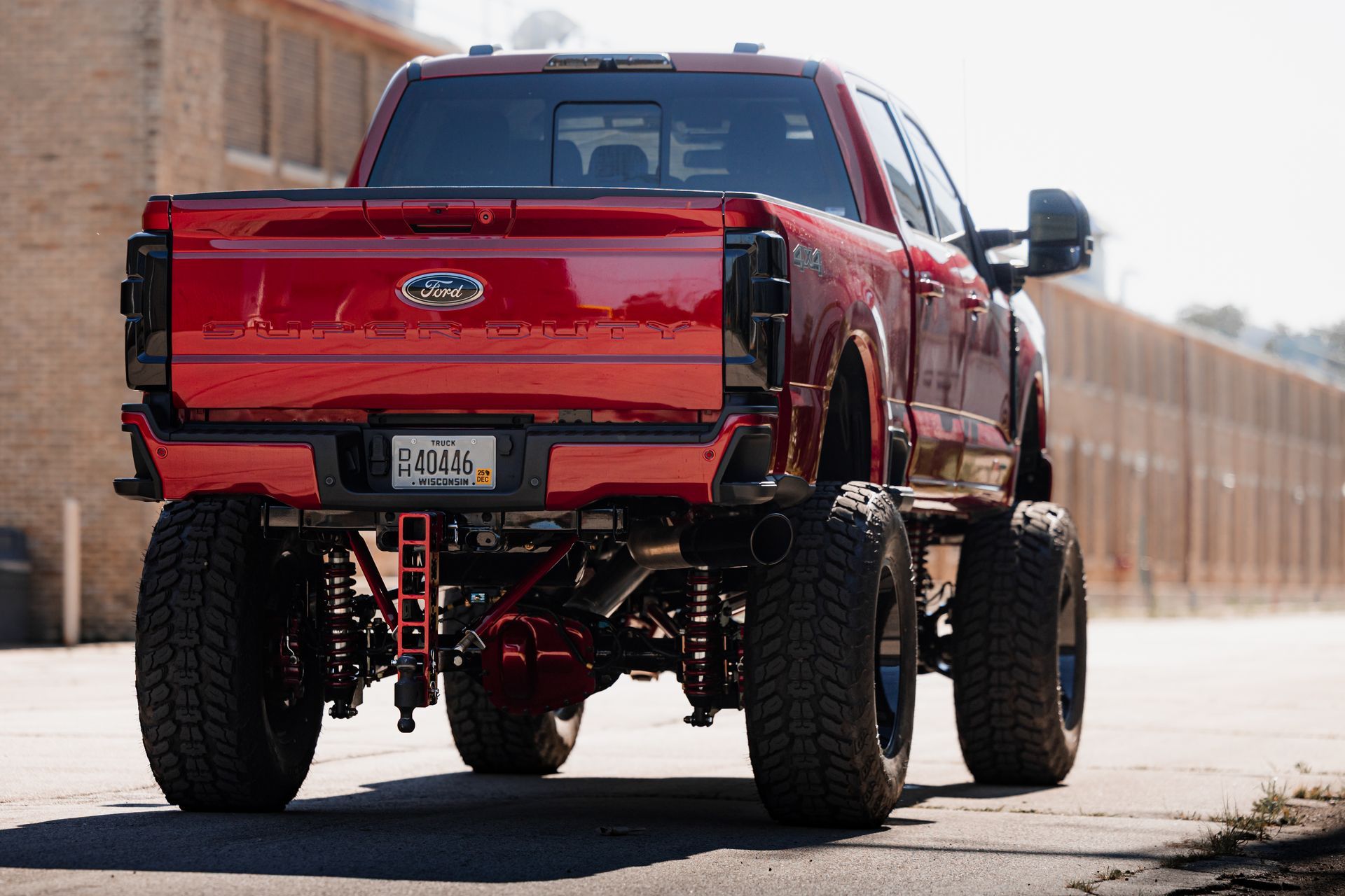 Red lifted Ford truck from the rear; black wheels, tinted tail lights, parked near a brick building.