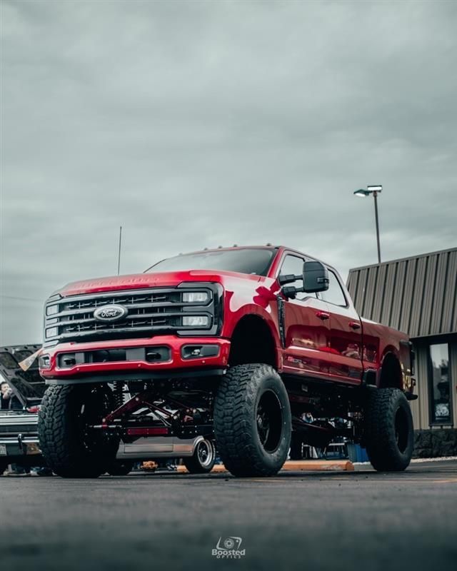 A red truck is parked in a parking lot in front of a building.