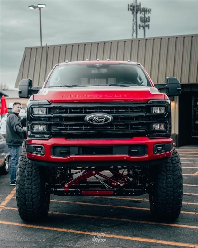 A red ford truck is parked in a parking lot in front of a building.