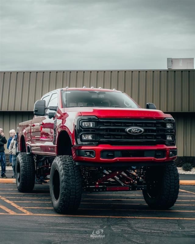A red ford truck is parked in a parking lot in front of a building.