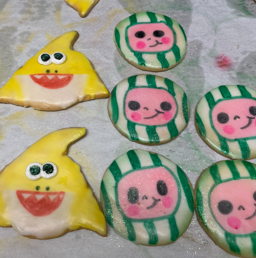Cute decorated cookies with yellow shark-like faces and green-striped pink faces on a tray