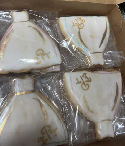 Four white-and-gold decorative cookie or dessert pieces in plastic wrap inside a box