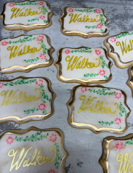 Decorated gold-and-white cookies with the name “Walker” on a gray surface