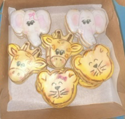 Box of decorated animal-shaped cookies, including elephant, giraffe, and cat faces, in a cardboard tray