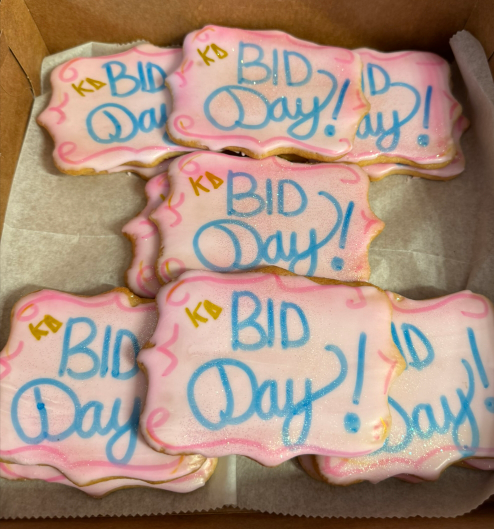 Box of pink-frosted cookies decorated with “Bid Day!” in blue and gold icing.