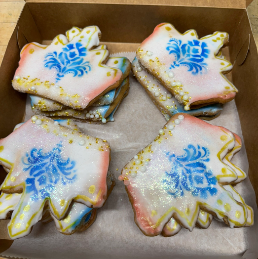 Four decorated iced cookies in a cardboard box, white with blue designs and pastel edges.