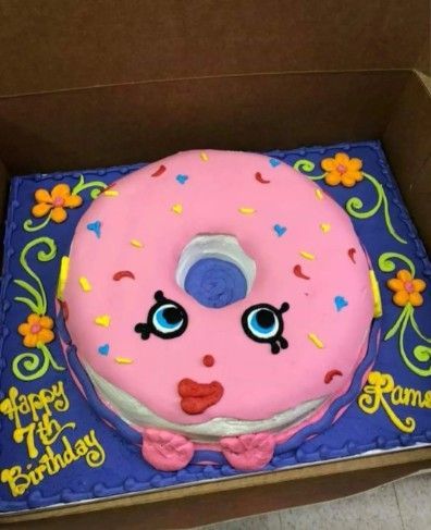 Pink frosted birthday cake with a cartoon face, flowers, and blue border in a box