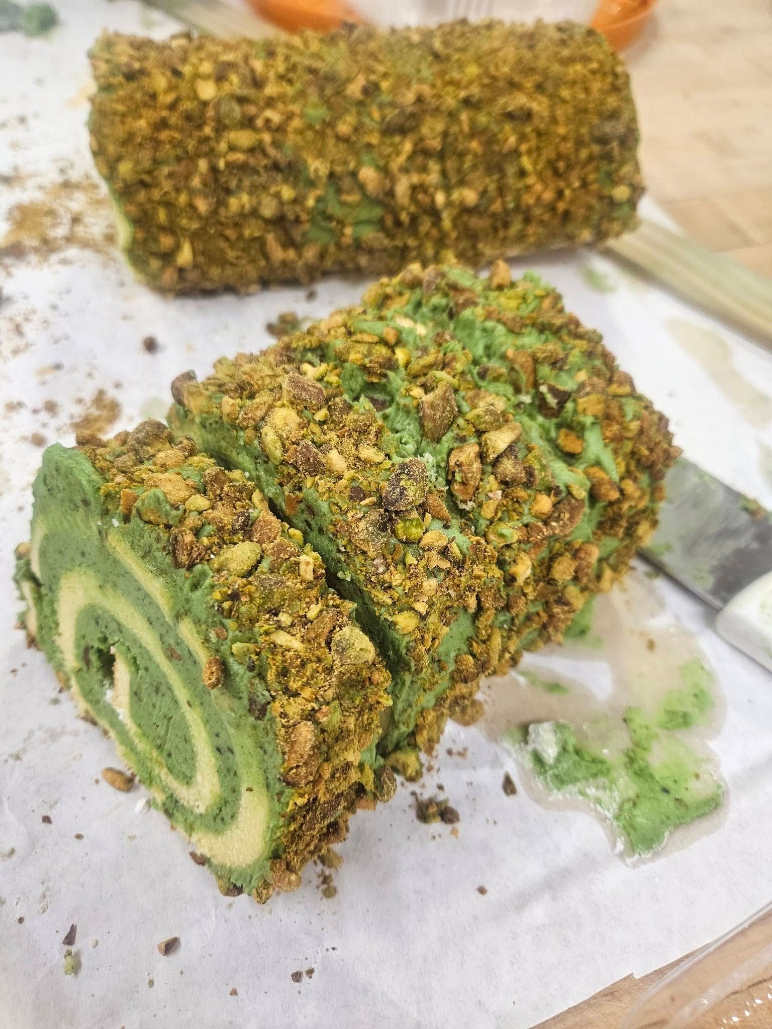 Green pistachio Swiss roll slices topped with chopped pistachios on parchment paper