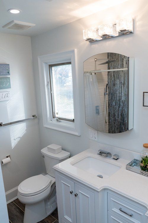 A bathroom with a toilet , sink , mirror and window.