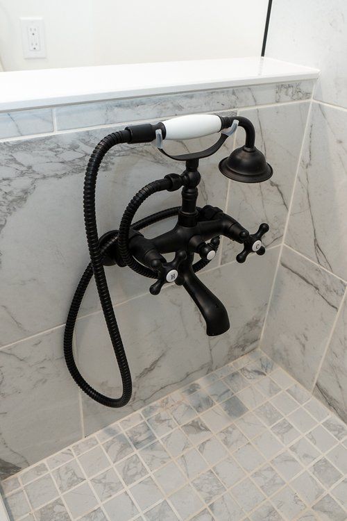 A black bathtub faucet with a white handle is hanging from the wall in a bathroom.