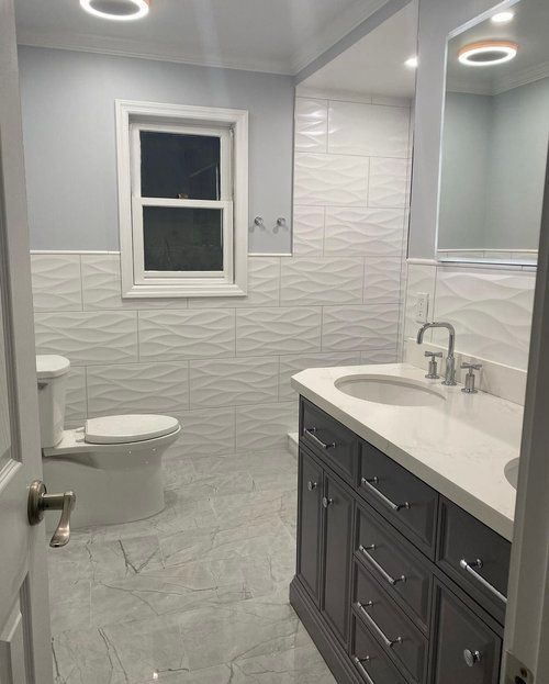 A bathroom with a toilet , sink , mirror and window.