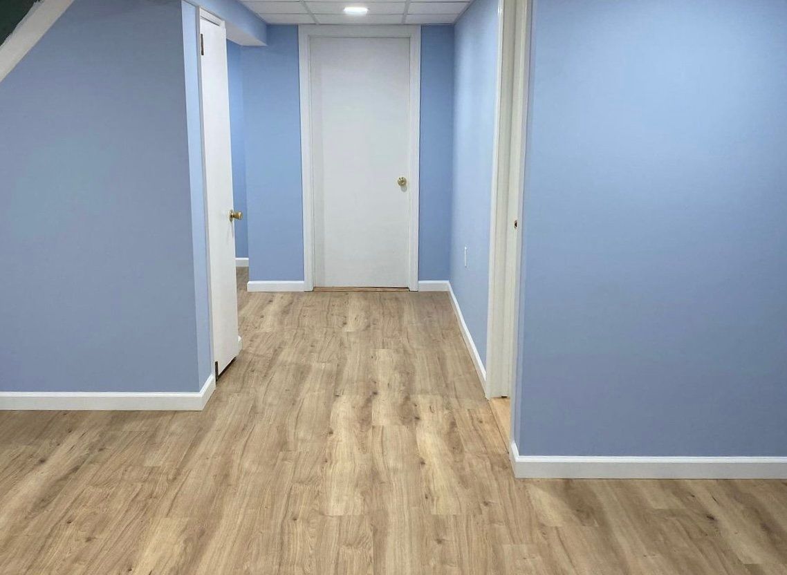 A hallway in a basement with blue walls and wooden floors.