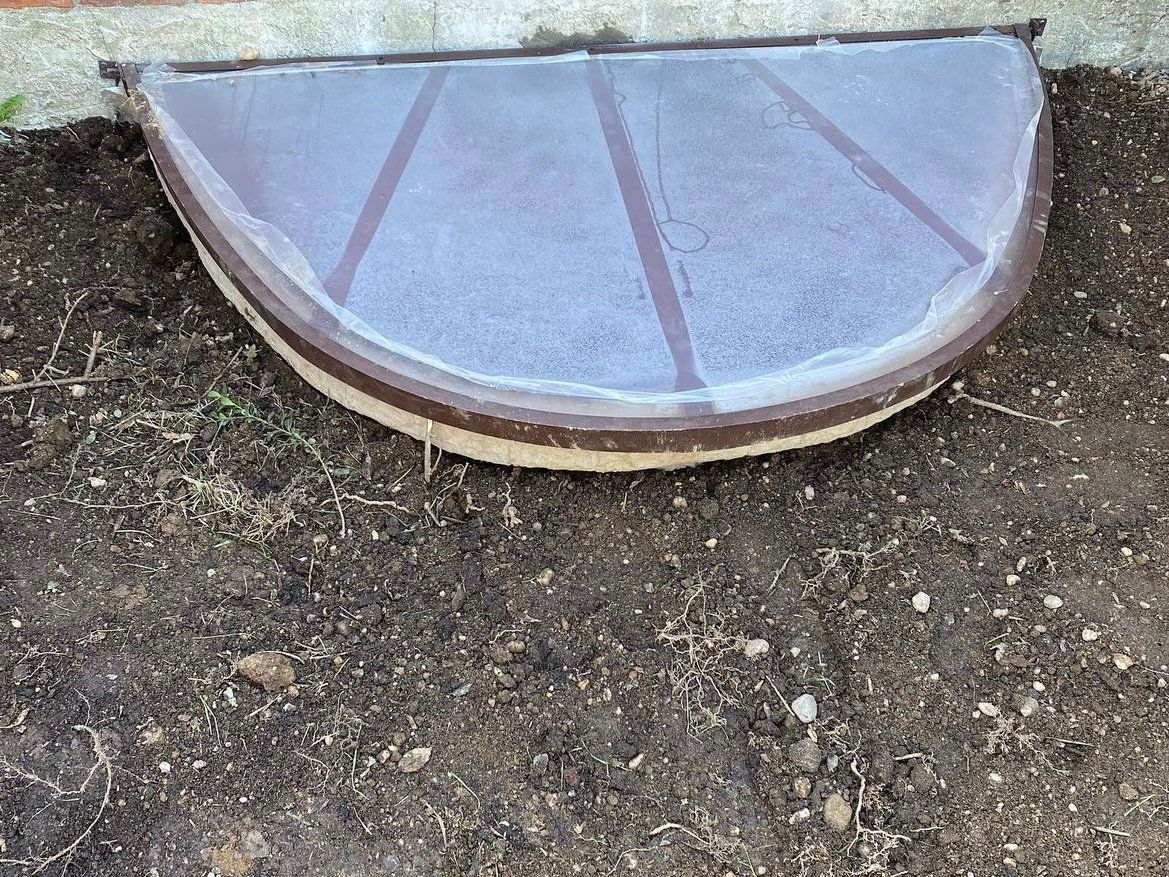 A window well with a screen on it is sitting in the dirt.