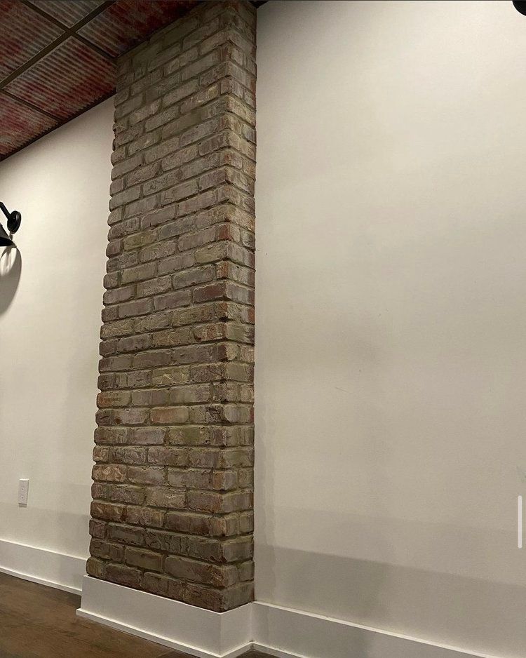 There is a brick wall in the corner of a room.